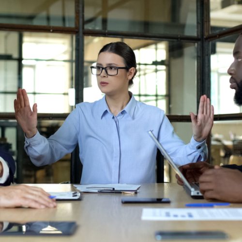 Female manager showing stop sign to arguing workers office, conflict resolution